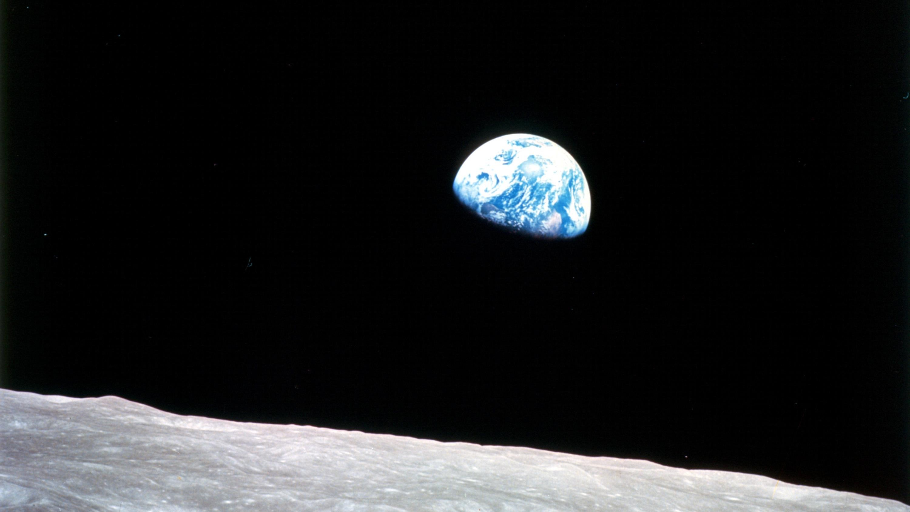 View of Earth rising over the Moon’s surface against a black space backdrop, captured during an Apollo mission.