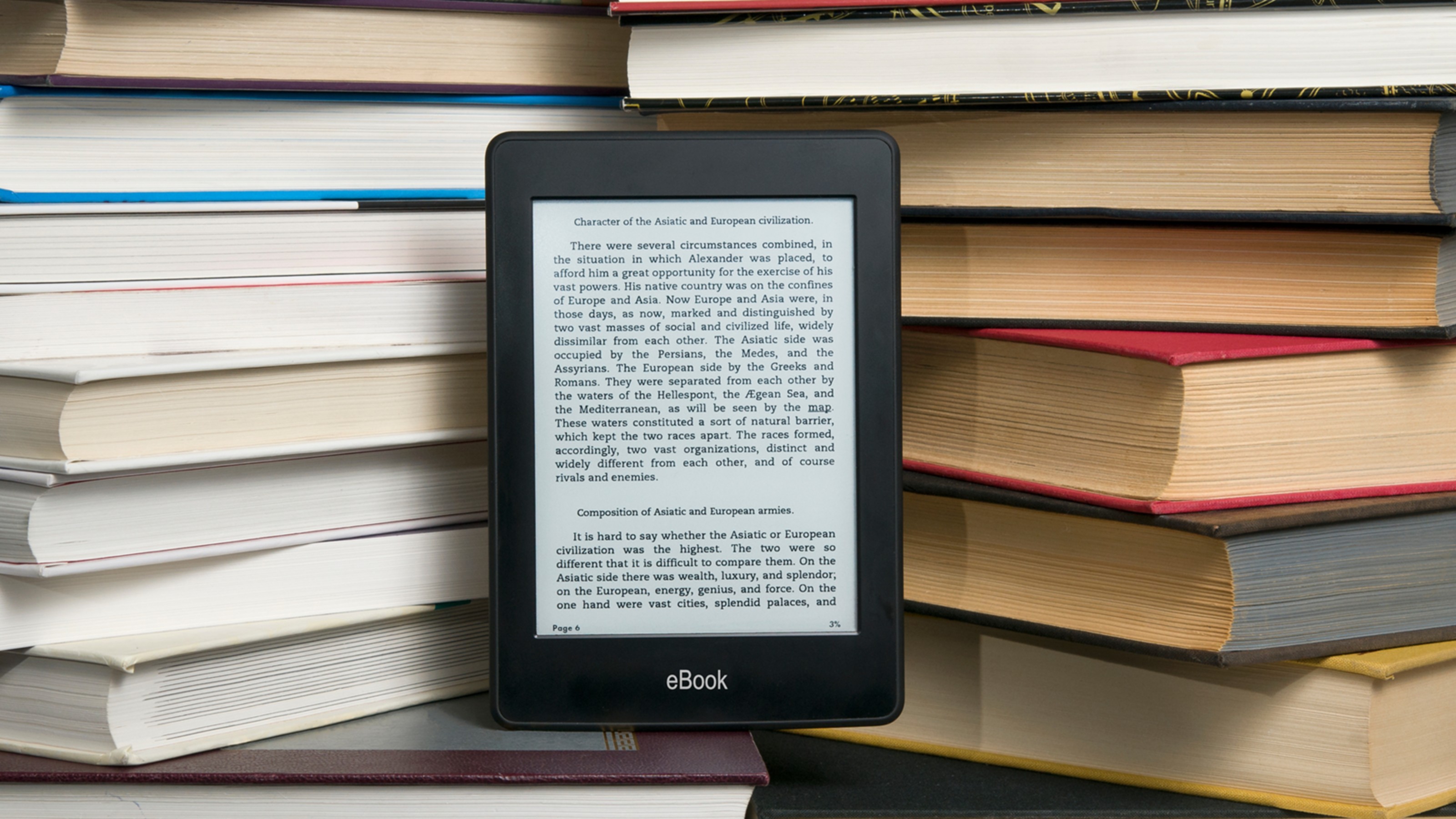 An e-reader displaying text is propped up against a stack of hardcover books.