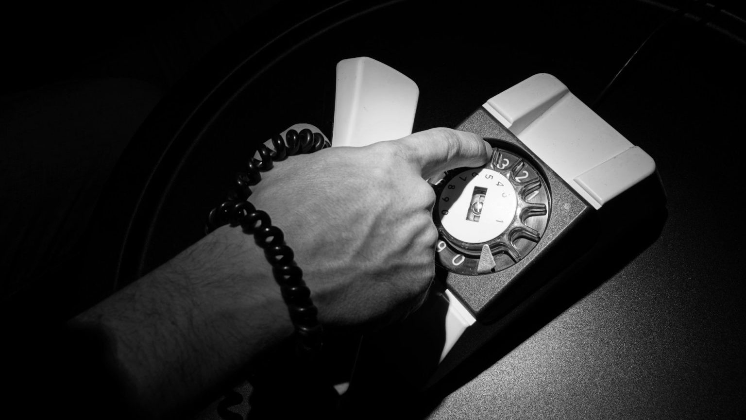 A hand with emotional intelligence dials a vintage rotary telephone, its coiled cord adding to the nostalgia of the black-and-white scene.