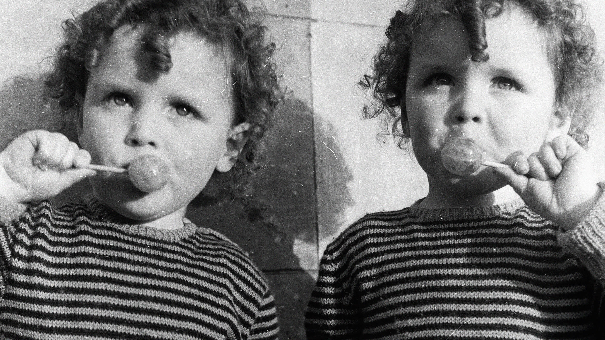 Two young children with curly hair in striped sweaters enjoy lollipops, showcasing the whimsical nature of genes and behavior. The black-and-white photo gives a nostalgic feel.